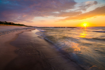 sunset over the sea beach, waves crashing on the stakes