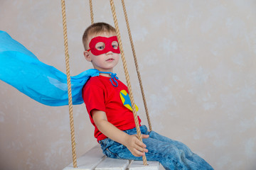 boy a superhero in a blue Cape on a swing