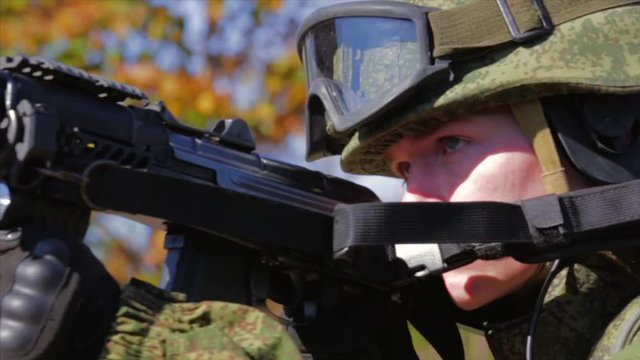 Soldier with modern equipment aiming with AK rifle. Closeup. Front view