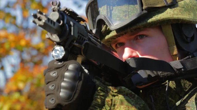 Military man. Young soldier aiming with automatic rifle. Closeup. Front view