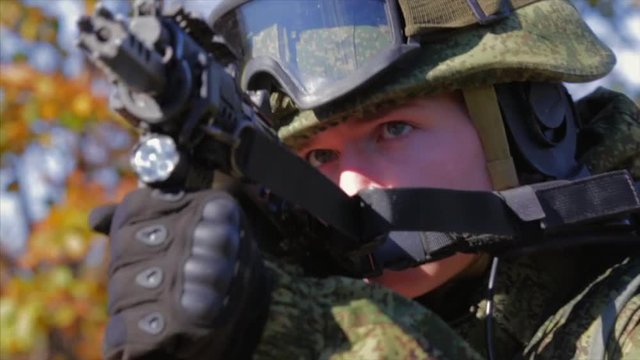Soldier with modern equipment aiming with AK rifle. Closeup. Front view