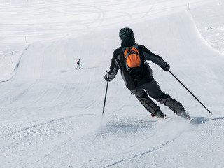 Skier in black downhill skiing on a ski slope. View from back.