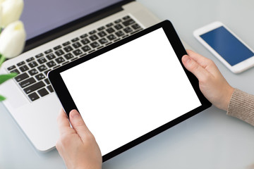 female hands holding tablet with isolated screen above laptop phone