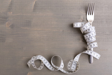 Diet concept, fork and measuring tape isolated on wooden background