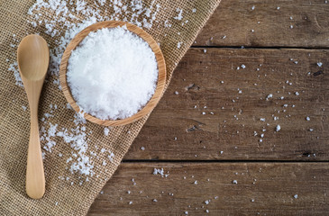 white sea salt in wood bowl with wood spoon on gunny sack cloth on brown wooden table, top view...