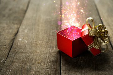 Red Christmas gift box with colorful magical lights on wooden desk.