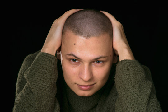 A young man is skinhead in a green military style sweater. studio.