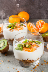 Healthy tangerine and kiwi yogurt granola dessert for breakfast, with ingredients, gray stone table, copy space