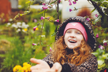 Happy laughing girl catches rain drops her hands in spring garden.