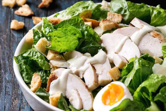 Classic Caesar salad with grilled chicken breast and half of egg in white ceramic plate. Over old dark blue wooden background. Close up. Rustic style