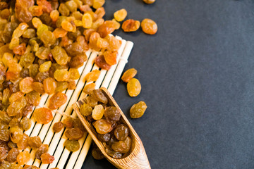 Raisins on a wooden spoon. Natural light. Selective focus. Close up on a black background. Top view, flat lay. copy space. dried grapes