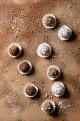 Variety of homemade dark chocolate truffles with cocoa powder, coconut, walnuts over cocoa powder as background. Top view, copy space.