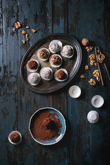 Variety of homemade dark chocolate truffles with cocoa powder, coconut, walnuts on vintage tray over old dark blue wooden background. Top view, space. Rustic style