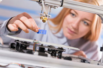 A female student or laboratory assistant in the automation laboratory is debugging the work of the 3d printer. 3d printer is a device for modeling 3D objects