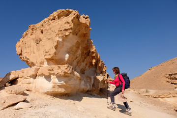 Middle aged female hiker climbing on yellow rock formation in Negev desert mountains.