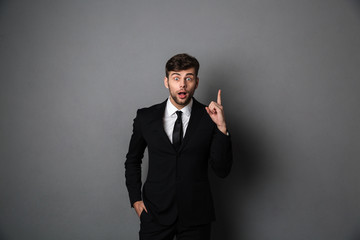 Amazed young man in suit pointing with finger upward, looking at camera