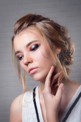 Obraz premium Girl blonde with a cocktail makeup on the eyes closed and hand raised to the chin on a light background