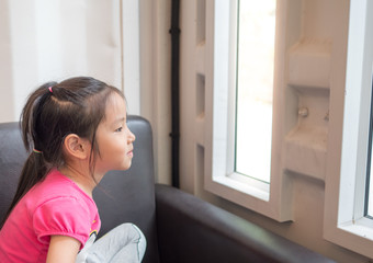 Beautiful little girl watching out the window. sit on the sofa