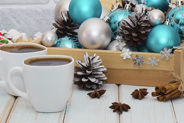 Decorative balls and pine cones in a wooden box and two white cups of coffee. The concept of Christmas and New Year.
