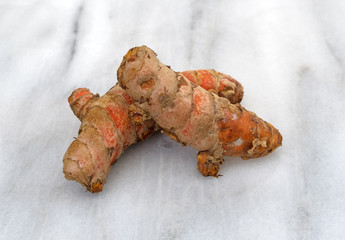 Two turmeric roots on a gray marble cutting board.