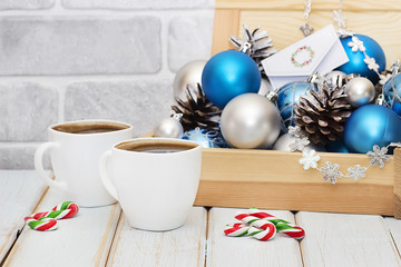 Decorative balls and pine cones in a wooden box and two white cups of coffee. The Christmas card.