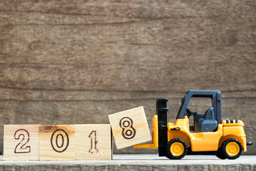 Toy plastic forklift hold block to compose and fulfill wording 2018 on wood background