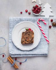 A piece of traditional Christmas English pudding (fruit cake) on white plate on a concrete light background. Christmas decor of the table.   Flat lay, top view