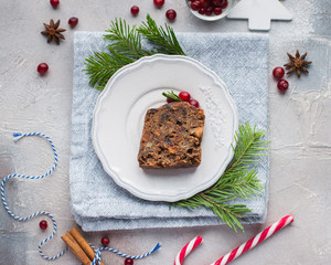 A piece of traditional Christmas English pudding (fruit cake) on white plate on a concrete light background. Christmas decor of the table.   Flat lay, top view