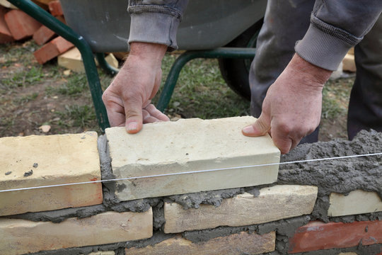 Mason building wall with mortar and bricks, closeup of hands