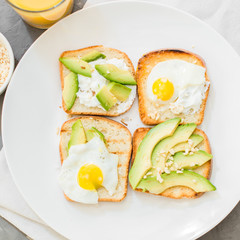 Breakfast. Eggs on toast with avocado, soft white cheese, spices and nuts. White plate, gray concrete background.
