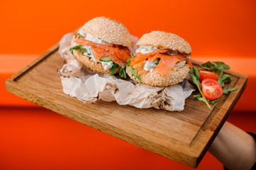 Cold burgers with salmon, sauce, cucumber, tomato and arugula served in the wooden plate