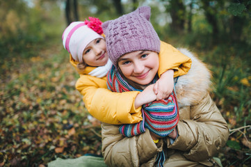 The younger sister hugs her older sister. Happy smiling children are having fun in the autumn park.