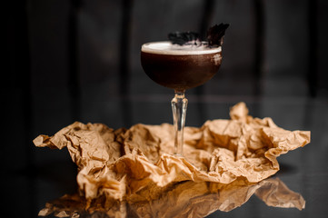 Cocktail glass with dark alcoholic drink decorated with basil leaf