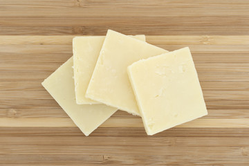 Top view of several slices of sharp cheddar cheese squares on a small wood cutting board.