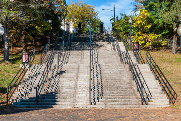 Outdoor concrete park steps. Parks and recreation design with tree and shrub background. Nature setting with stone stairwell and railings.