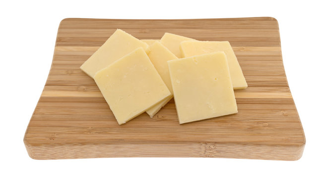 Several slices of sharp cheddar cheese squares on a small wood cutting board isolated on a white background.