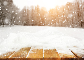 Wooden desk covered by snow and snowy park on background