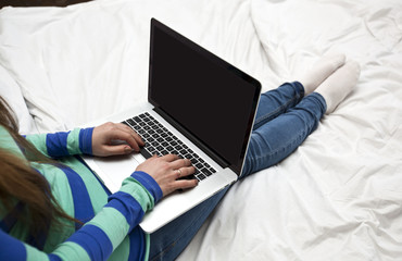 Naklejka premium The young woman is lying on the bed with a laptop