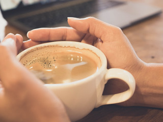 Nahaufnahme der Hände halten eine weiße Tasse schwarzen Kaffee auf Holztisch im Kaffeecafé
