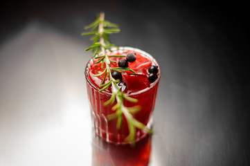 Glass of a red alcoholic drink decorated with a sprig of rosemary and black currant berries