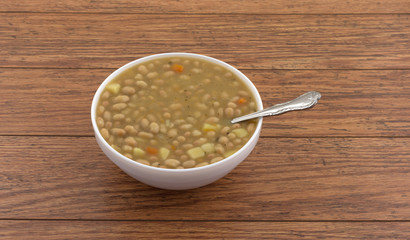 A white bowl filled with bean and carrot soup with a spoon in the food on an old wood table.