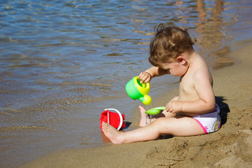 A baby plays near the sea with water and sand