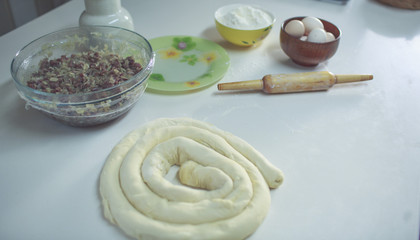 on a white table a bowl with eggs and flour, ready to be rolled up and next to the rolling pin. view from above