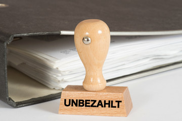 Ein Ordner Rechnungen und ein Stempel mit dem Aufdruck Unbezahlt