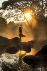 Silhouette of a beautiful Yoga woman in the morning at the hot spring park,
