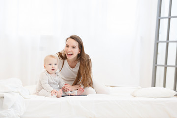 portrait of young happy mother and her little son in white home clothes and in a light bedroom before bedtime. look at camera. White pajamas, happy childhood. Copy space
