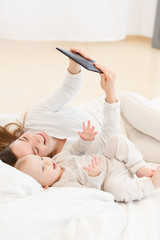 young mother happy spends time with her little baby boy and watch animated films on the tablet in a...
