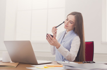 Business woman refreshing her makeup at office