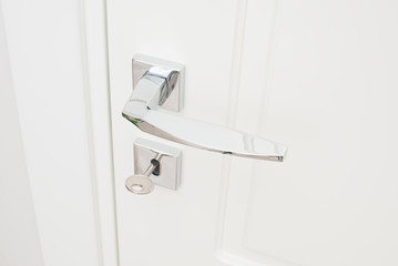 Modern glossy chrome door handle and keyhole with key. Close-up elements of the interior of the apartment.