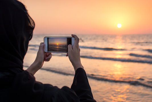 Woman in hijab taking picture of a sunset